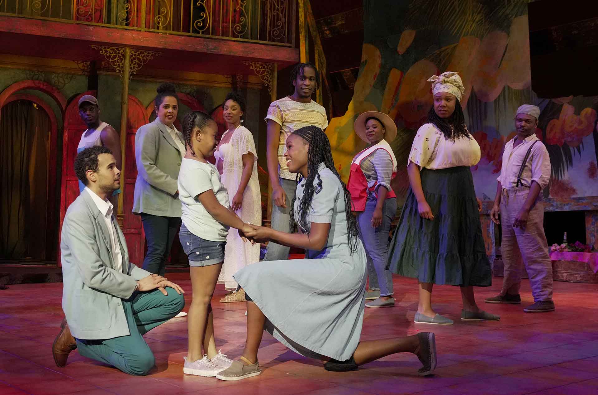 A person kneeling, smiling at a child with the ensemble standing in the background.