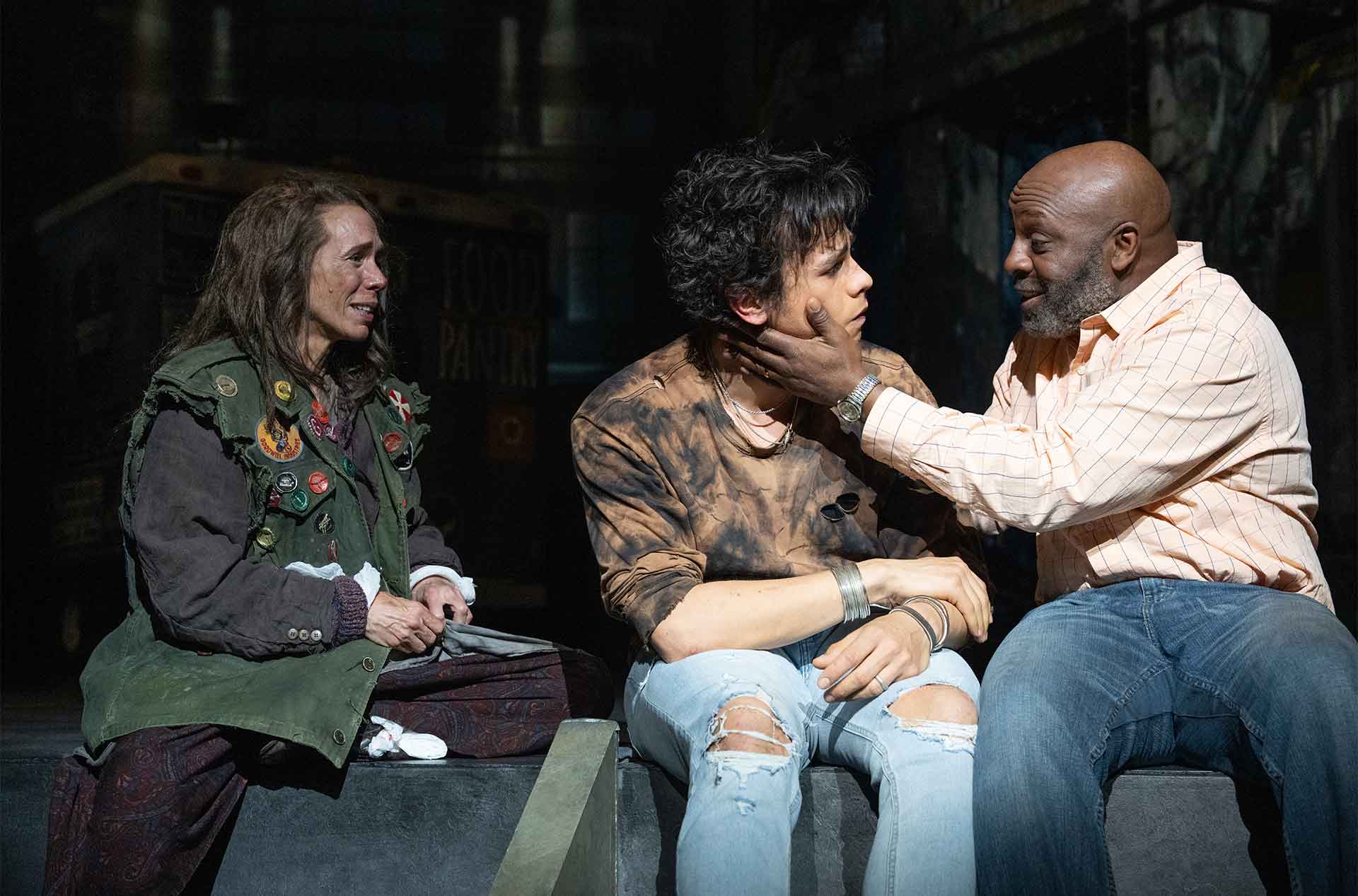 Three people sitting and talking with one of them holding another one's face.