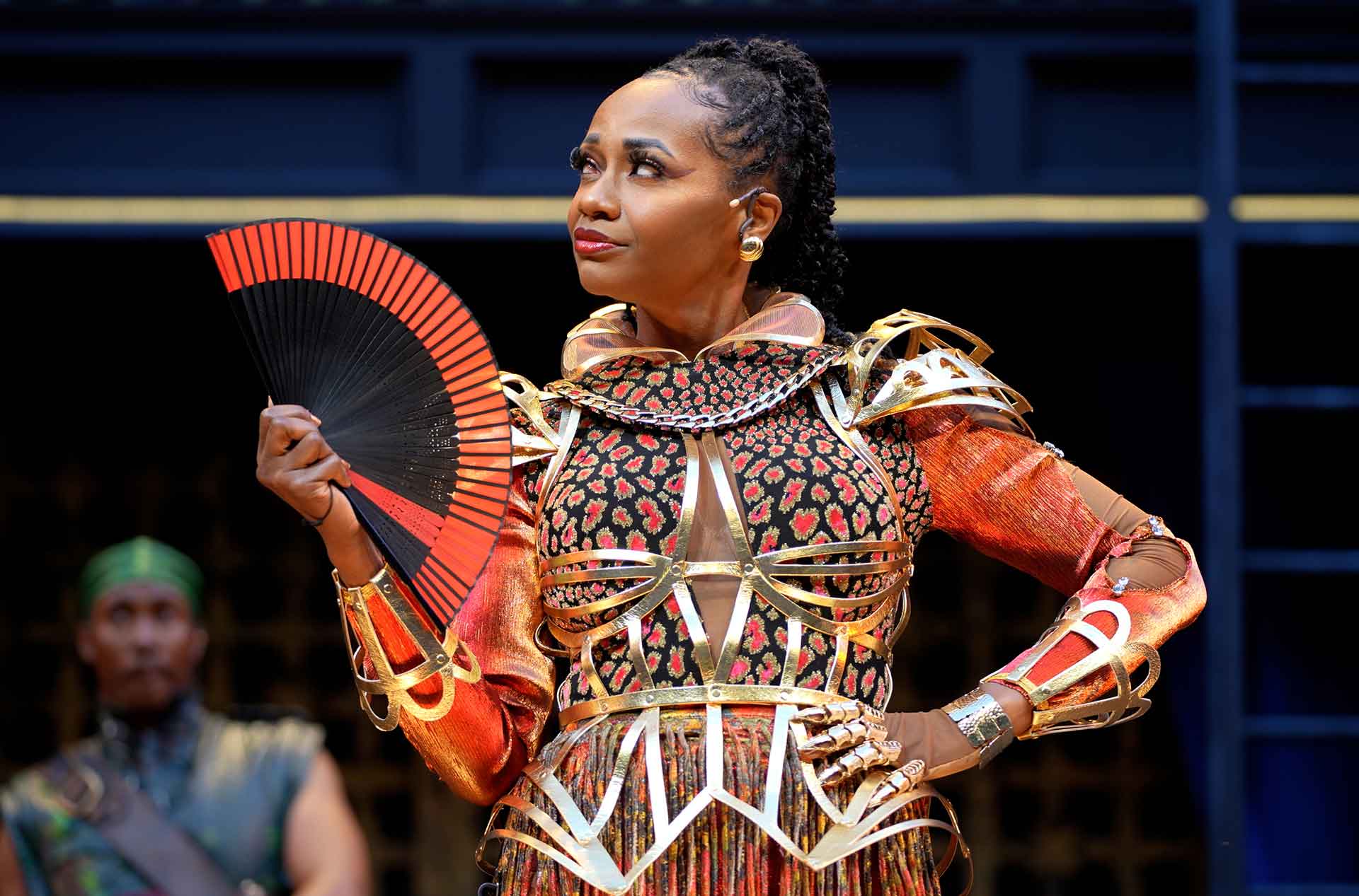 Person standing with a fan and a hand on their hip.