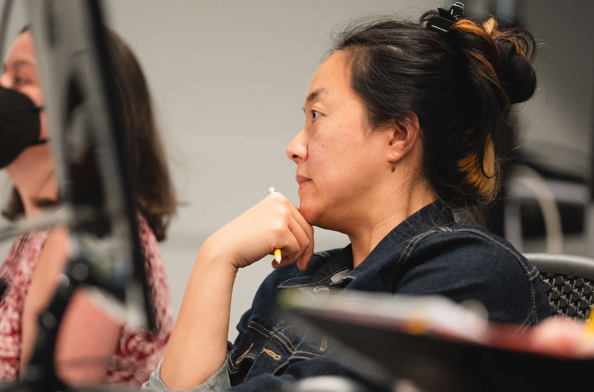 Person with a thoughtful expression sits in front of a computer monitor, holding a pen to their chin.