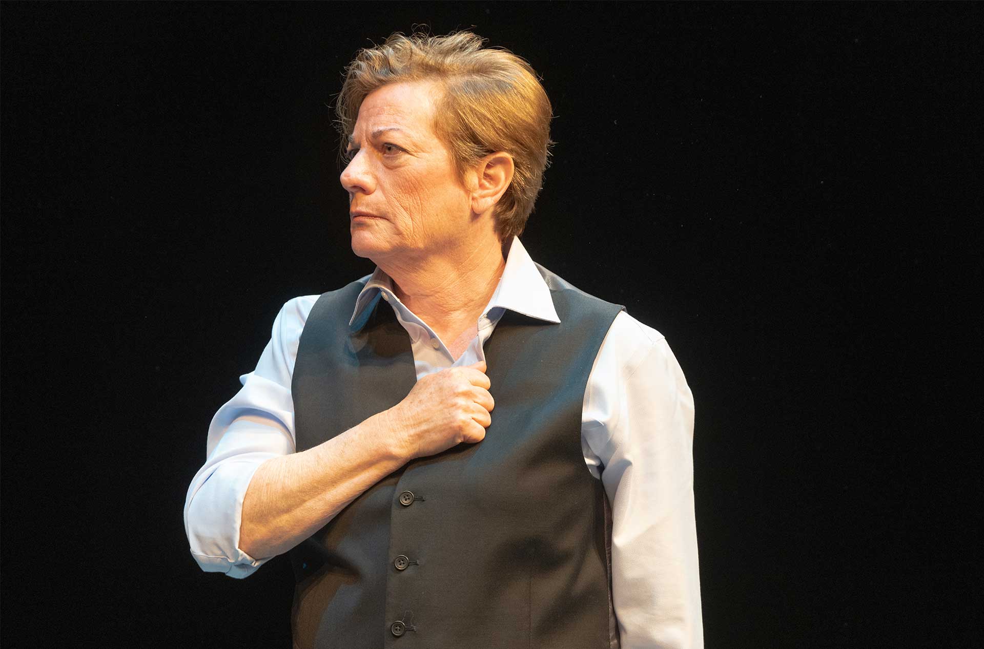 A person standing before a dark background with their fist covering their heart.