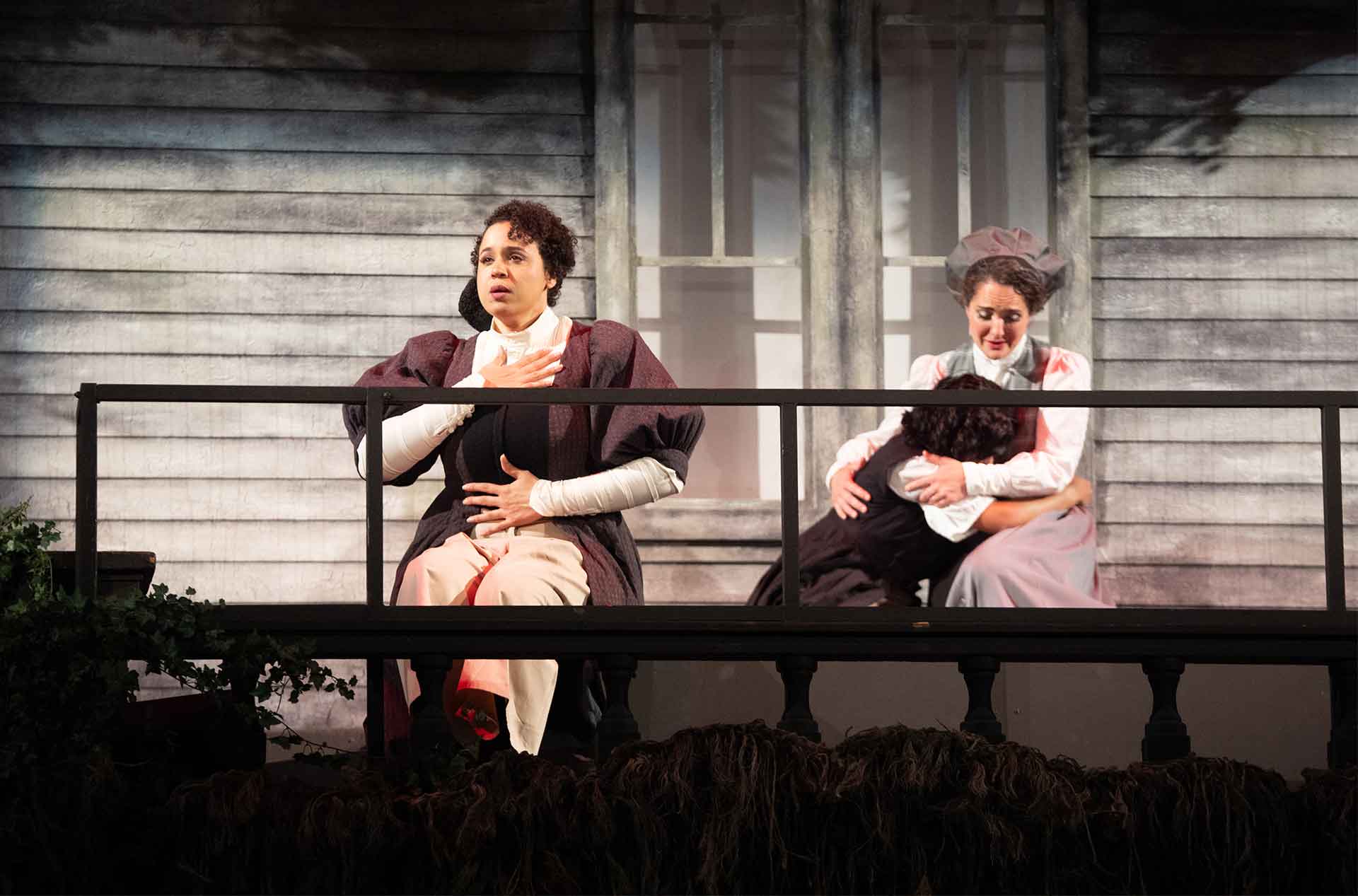 A person looking over a railing with their hands on stomach and chest while a person sitting in a chair is holding another with their face buried in their lap .