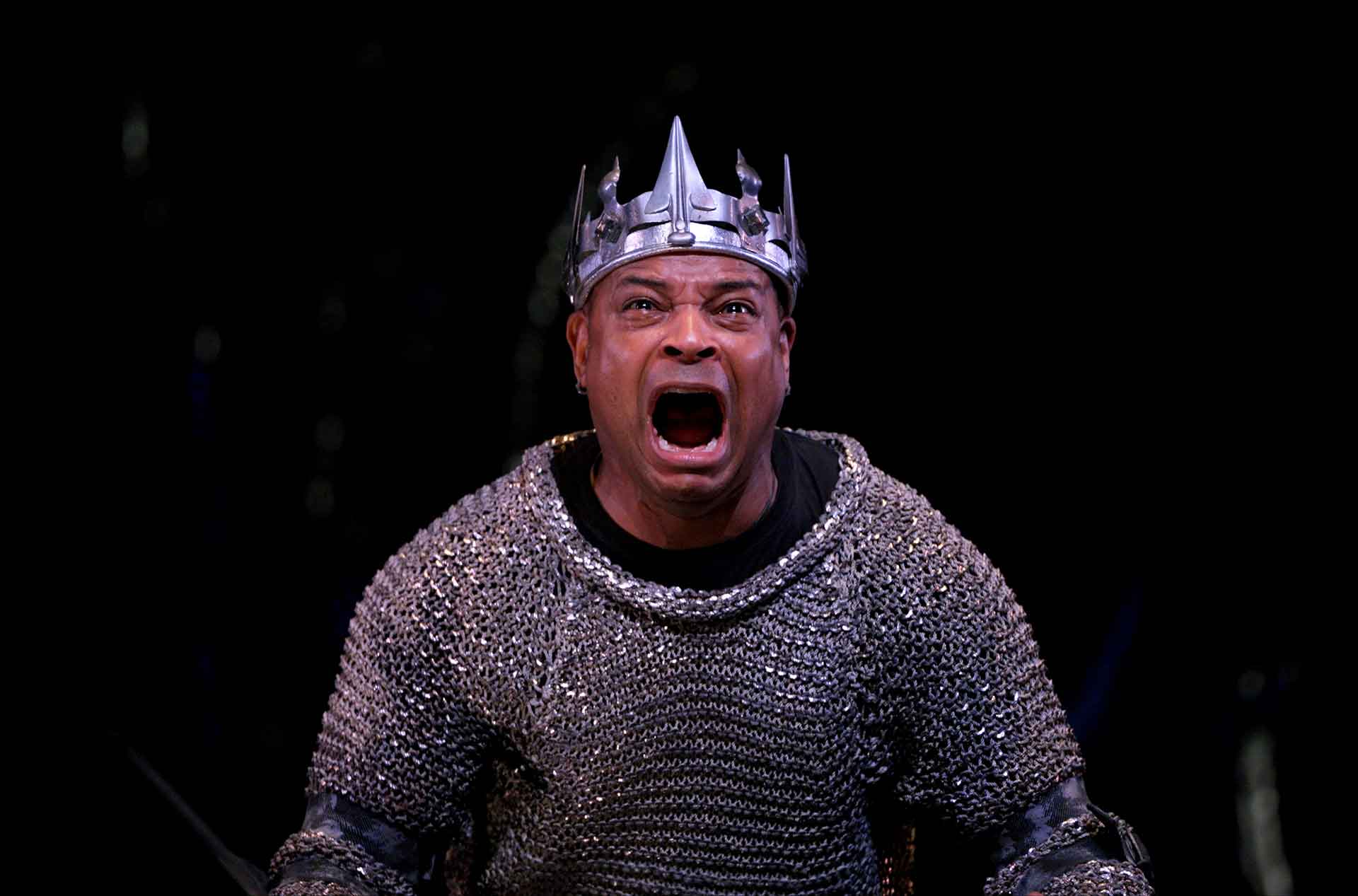 A king wearing a crown yelling out in despair.