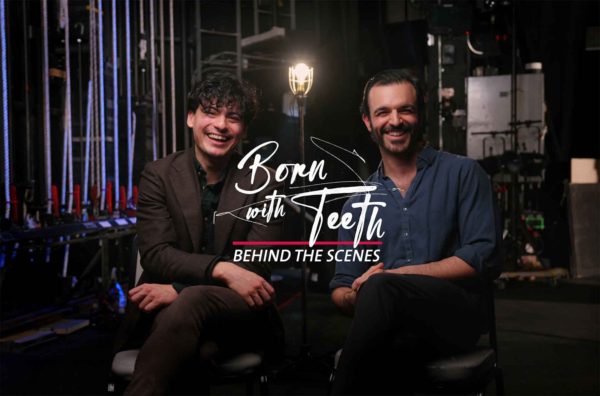 Two people sitting on a set smiling.