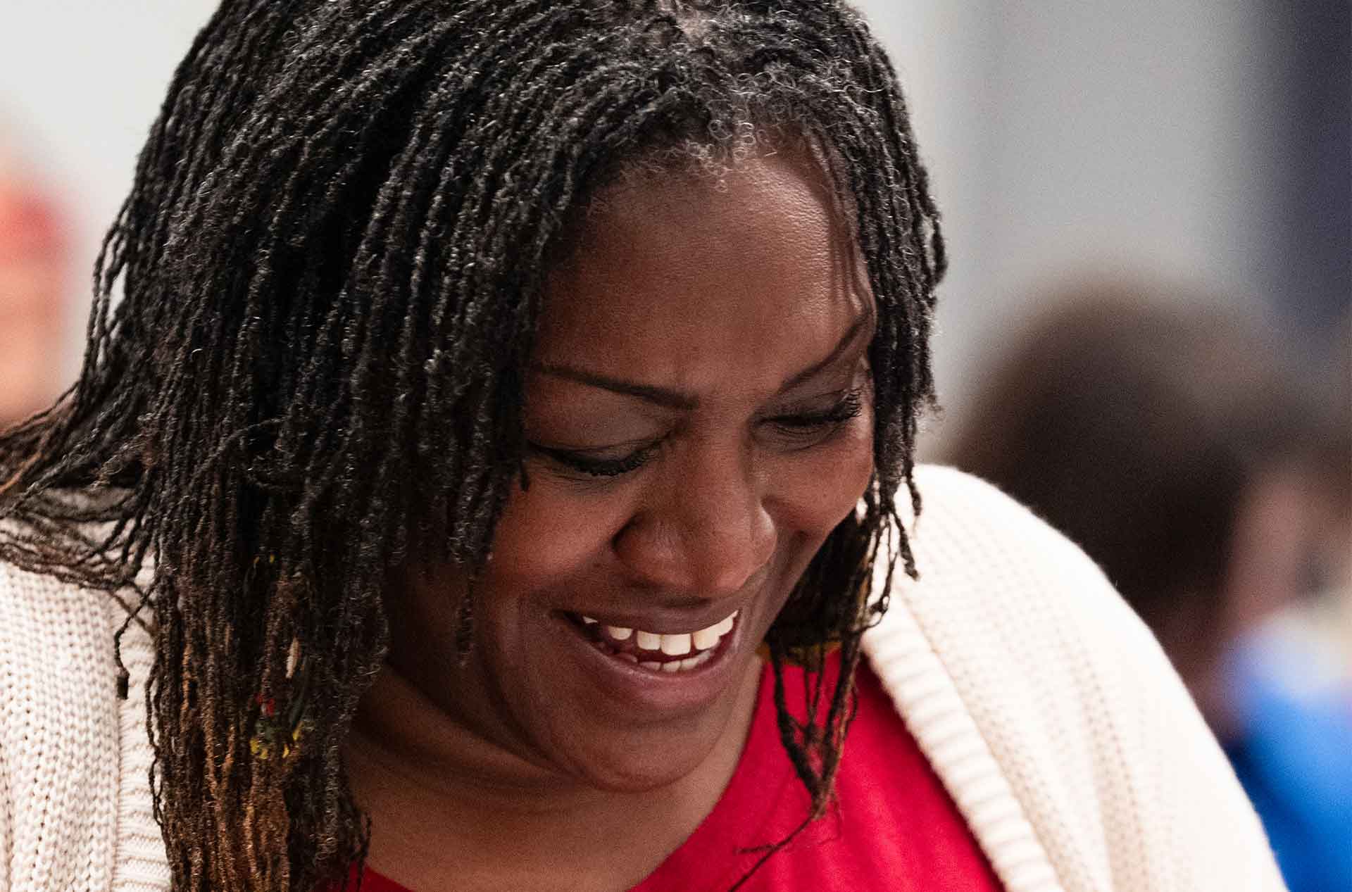 A person in a red top and a cream cardigan laughs while looking down at the table. Their hand is gesturing mid-conversation.