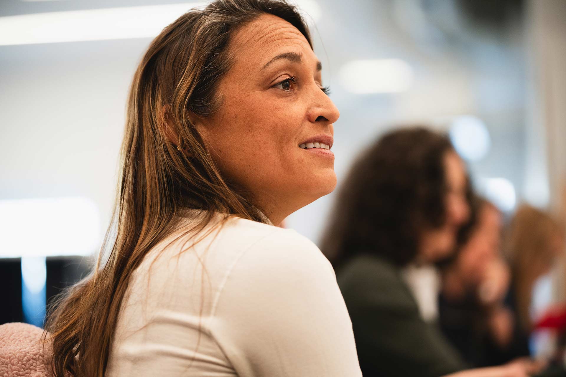 A rehearsal participant listens attentively during the discussion. They are seated in profile, with several people blurred in the background.