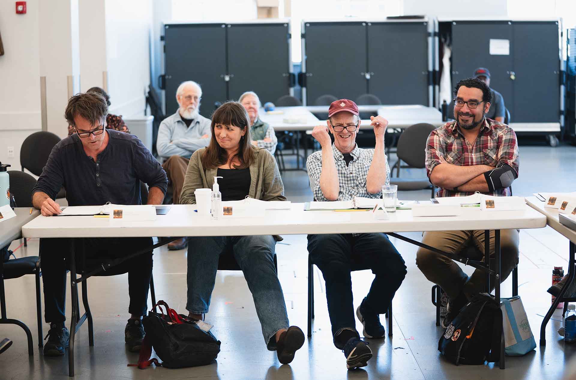 Four people sit behind a long table with open notebooks and name placards.