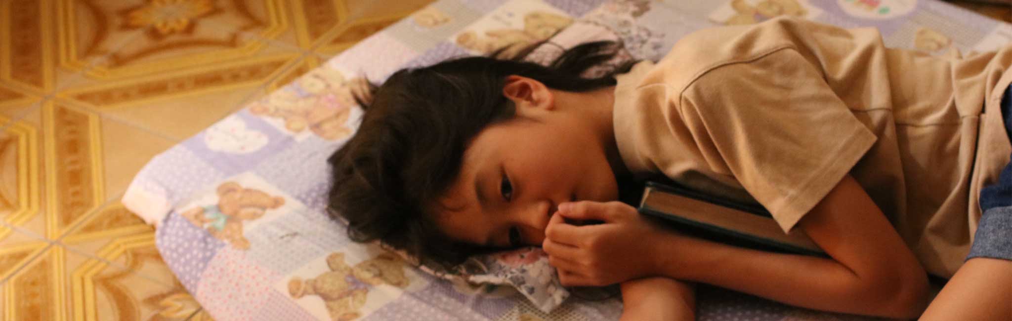 A girl laying on the floor on her side holding onto a book.