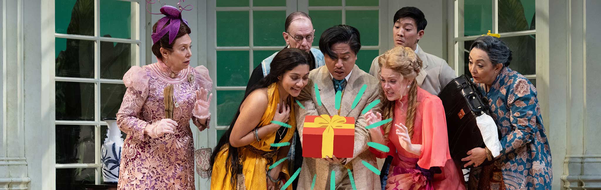 A group of seven people dressed in vintage costumes are gathered around a gift box with a festive bow, all expressing surprise and curiosity. The scene is set in an elegant, light-filled room with large windows.